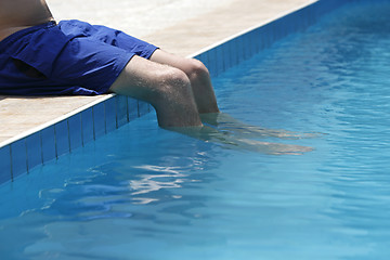 Image showing Attractive man with blue swimsuit sitting on the edge of the poo