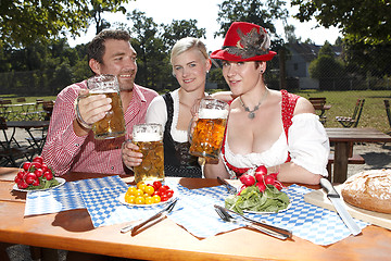 Image showing Three Bavarians in traditional costumes sitting in a beer garden