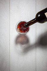 Image showing Red wine pouring into glass from bottle on white wooden table. T