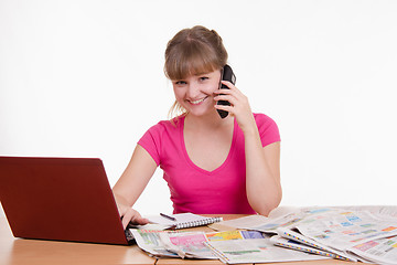 Image showing Girl talking on phone while sitting at a table with laptop