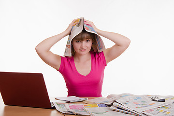 Image showing The girl at the table with a newspaper on his head