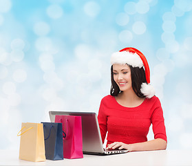 Image showing smiling woman in santa hat with bags and laptop