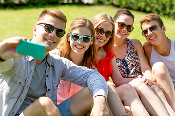 Image showing smiling friends with smartphone sitting on grass