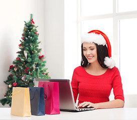 Image showing smiling woman in santa hat with bags and laptop