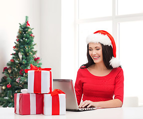 Image showing smiling woman in santa hat with gifts and laptop