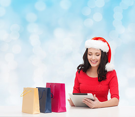 Image showing smiling woman in santa hat with bags and tablet pc