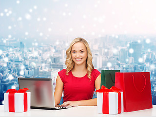 Image showing smiling woman in red shirt with gifts and laptop