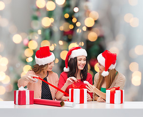 Image showing smiling women in santa helper hats packing gifts