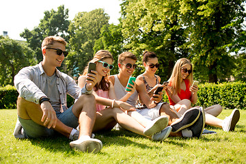 Image showing smiling friends with smartphones sitting on grass