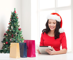 Image showing smiling woman in santa hat with bags and tablet pc