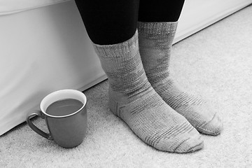 Image showing Hot drink on the floor by feet in socks