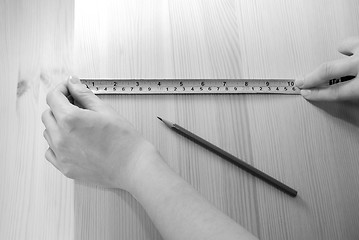 Image showing Two hands measure a wooden board with a steel tape measure