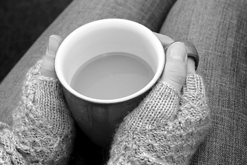 Image showing A woman in a cosy jumper holds a cup of tea or coffee on her lap