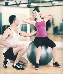 Image showing male trainer with woman doing crunches on the ball