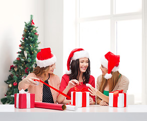 Image showing smiling women in santa helper hats packing gifts