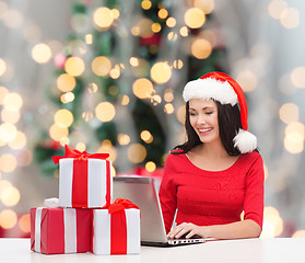 Image showing smiling woman in santa hat with gifts and laptop