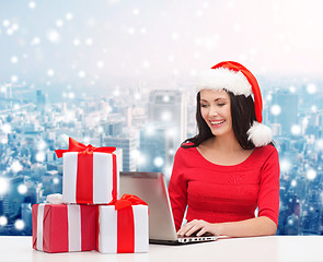Image showing smiling woman in santa hat with gifts and laptop