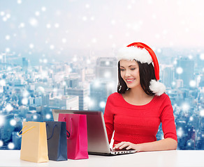 Image showing smiling woman in santa hat with bags and laptop