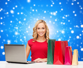 Image showing smiling woman in red dress with gifts and laptop