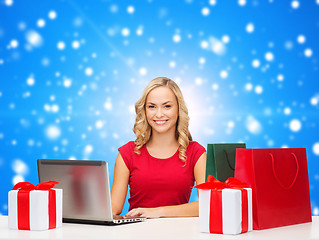 Image showing smiling woman in red shirt with gifts and laptop