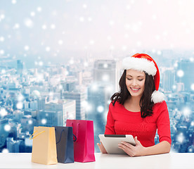 Image showing smiling woman in santa hat with bags and tablet pc