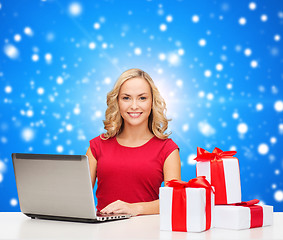 Image showing smiling woman in red shirt with gifts and laptop