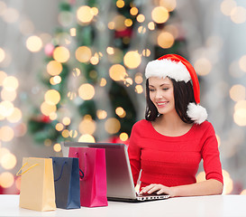 Image showing smiling woman in santa hat with bags and laptop