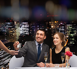 Image showing smiling couple paying for dinner with credit card