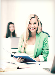 Image showing smiling young woman reading book at school