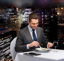 Image showing smiling man with tablet pc eating main course