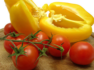 Image showing Halved yellow pepper and tomatoes on wooden plate  with knife