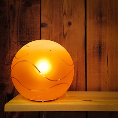 Image showing Cozy orange lamp on wooden shelf