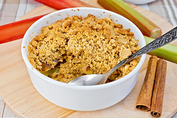 Image showing Crumble with rhubarb in bowl on linen tablecloth and board