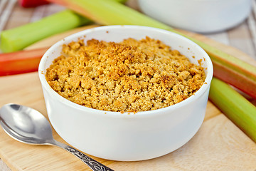 Image showing Crumble with rhubarb in bowl on tablecloth and board
