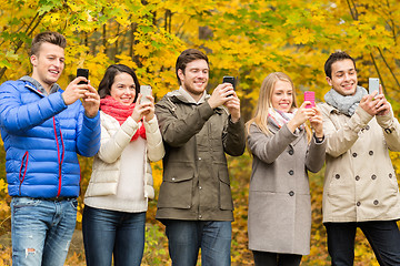 Image showing smiling friends with smartphones in city park