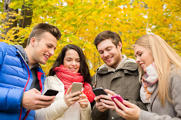 Image showing smiling friends with smartphones in city park