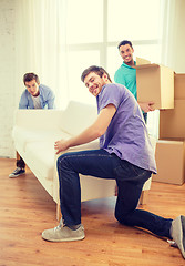 Image showing smiling friends with sofa and boxes at new home