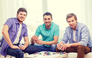 Image showing happy three male friends playing poker at home