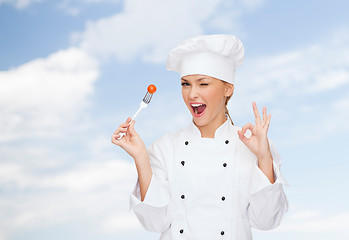 Image showing smiling female chef with fork and tomato