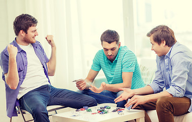 Image showing happy three male friends playing poker at home