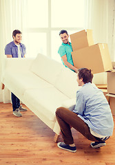 Image showing smiling friends with sofa and boxes at new home