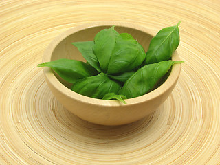 Image showing Wooden bowl with basil on bamboo plate