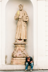 Image showing Homeless Old Man Sitting Outdoors Under A Statue Of A Monk In Pr