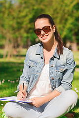 Image showing smiling young girl with notebook writing in park