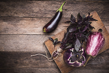 Image showing Tasty Aubergines and basil on chopping board and wooden table