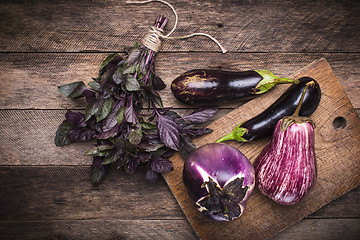 Image showing Aubergines and basil on chopping board and wooden table