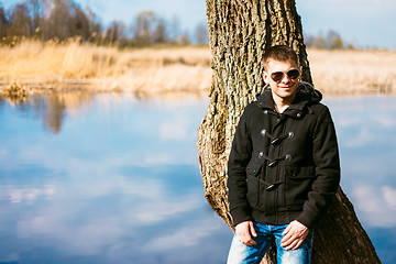 Image showing Young Handsome Man Leaned Against Tree By River In Autumn Day. C