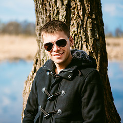 Image showing Young Handsome Man Leaned Against Tree By River In Autumn Day. C