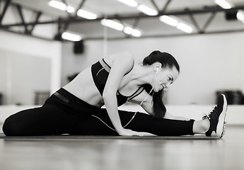 Image showing smiling woman stretching on mat in the gym