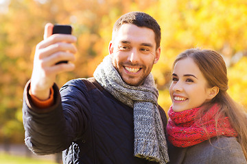 Image showing smiling couple with smartphone in autumn park